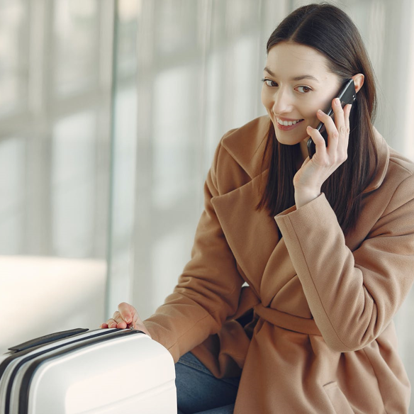 Dark haired woman in a tan coloured coat, talking on the phone
